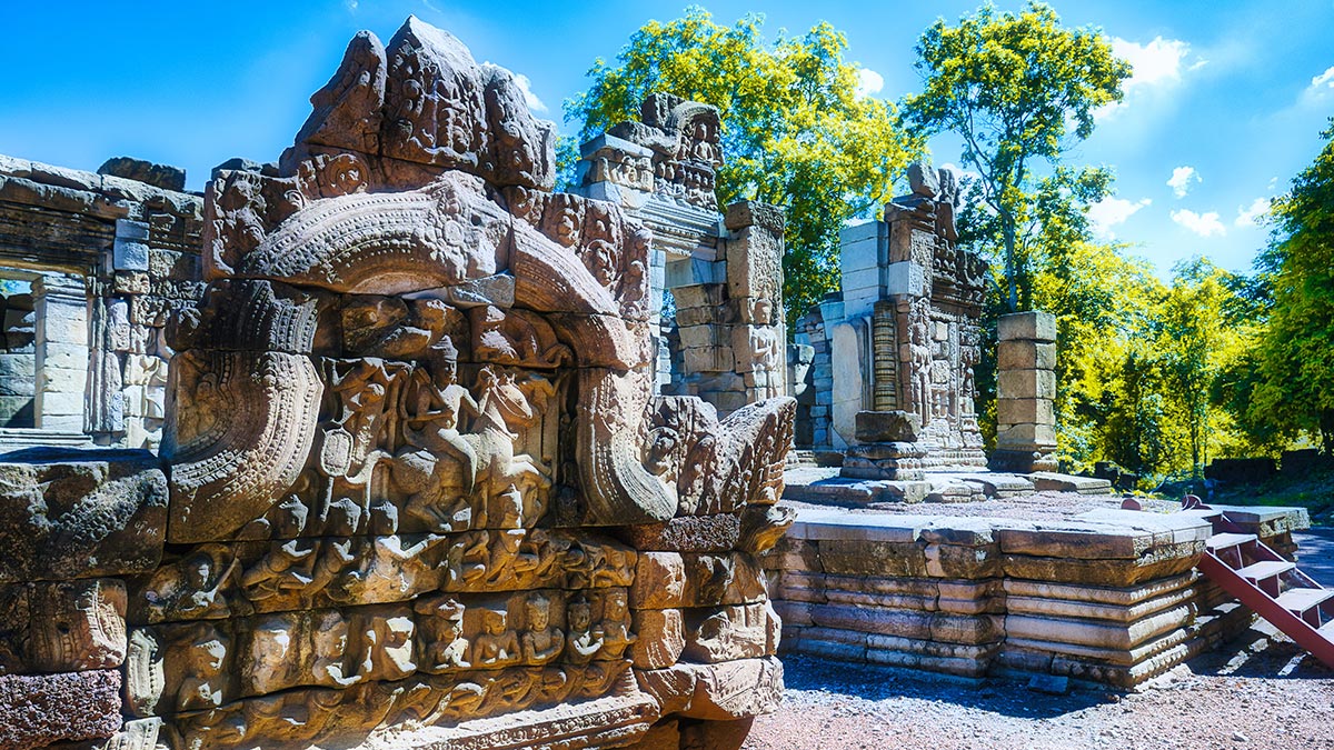 Kamenná buddhistická sochařská stavba s reliéfy, sloupy a schodištěm pod modrou oblohou.